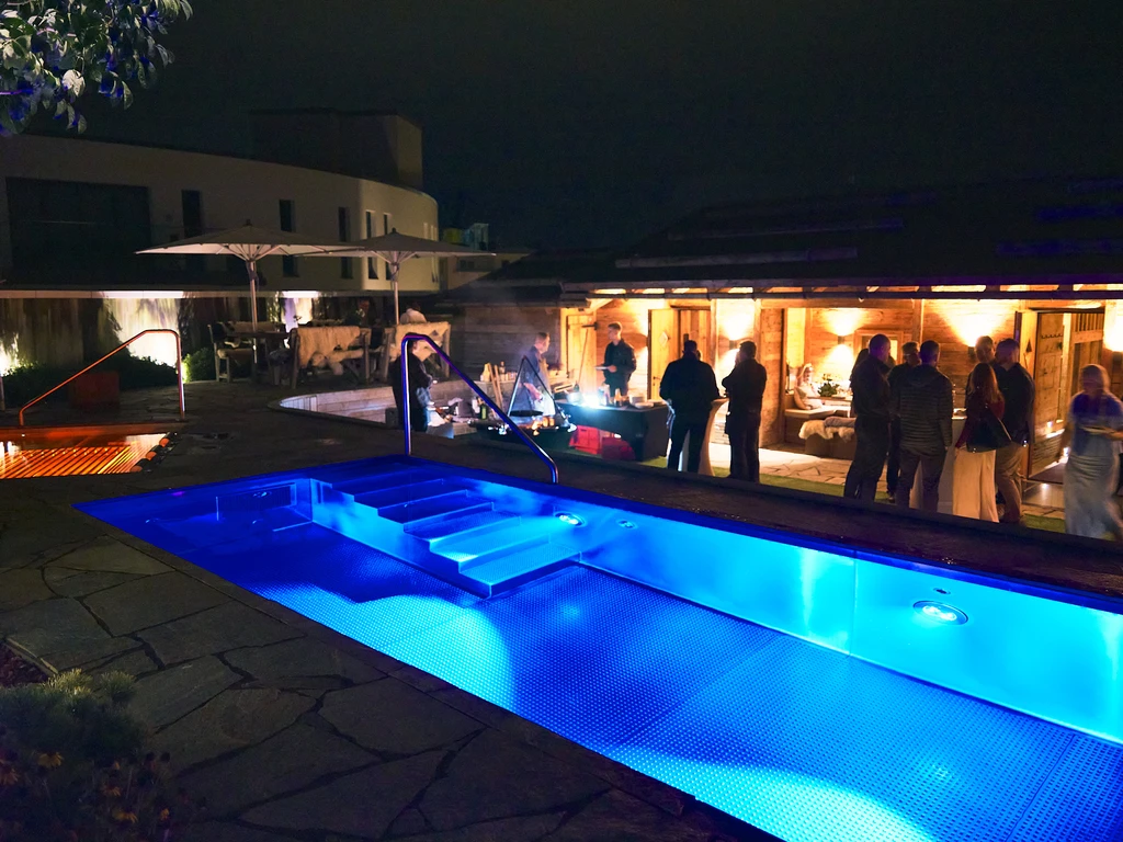 Die beleuchtete Dachterrasse des Chalet O bei Nacht mit Pool, Feuerring und Gästen vor der Hütte