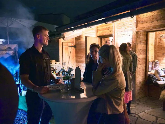 Gäste an einem Stehtisch vor der Hütte am Abend