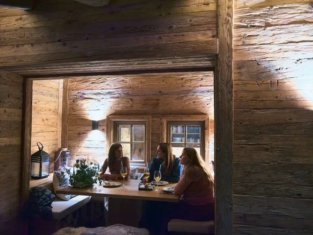 Drei Gäste im Gespräch am Holztisch in der Hütte