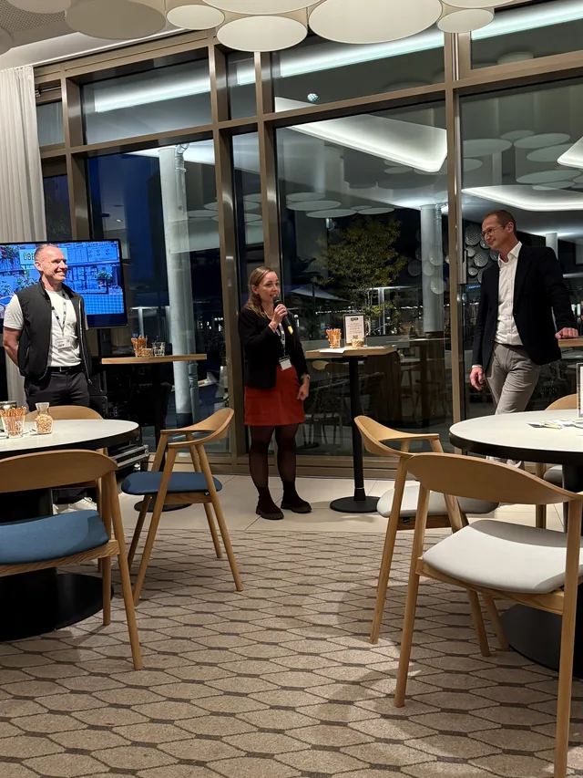 Begrüßung in der Lobby: die Gastgeberin spricht zu den Gästen, hinten die Glasfront zum Hafen