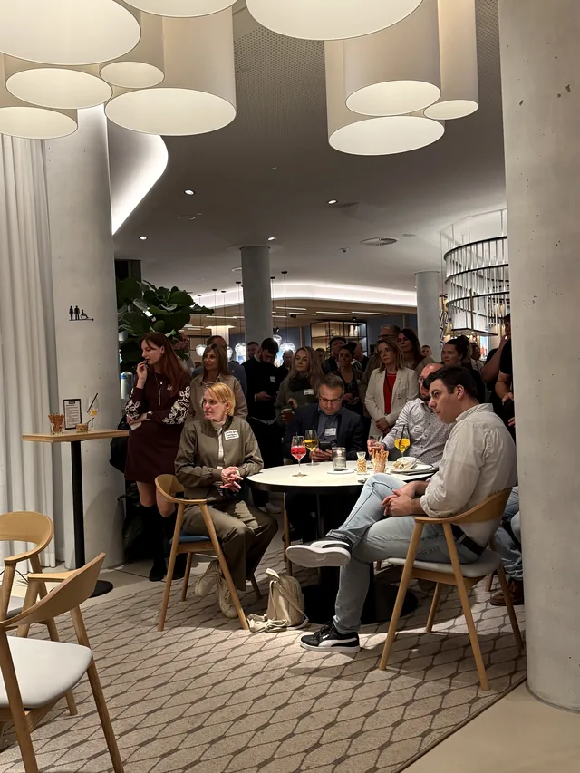 Volle Lobby mit runden Leuchten, Gäste an Stehtischen und Sitzgruppen